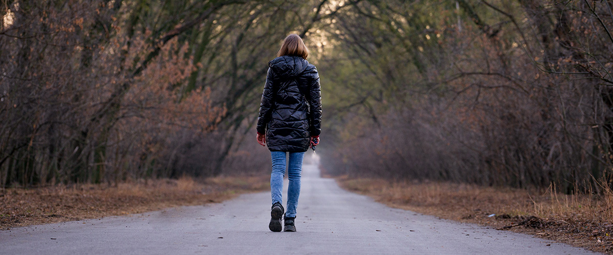 Persona caminando sola hacia un camino luminoso, dejando atras un entorno oscuro y caotico, representando la importancia de distanciarse de estimulos perjudiciales.